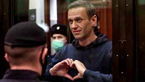 Alexei Navalny makes the shape of a heart with his hands while standing inside a glass cell during a court hearing in Moscow in 2021